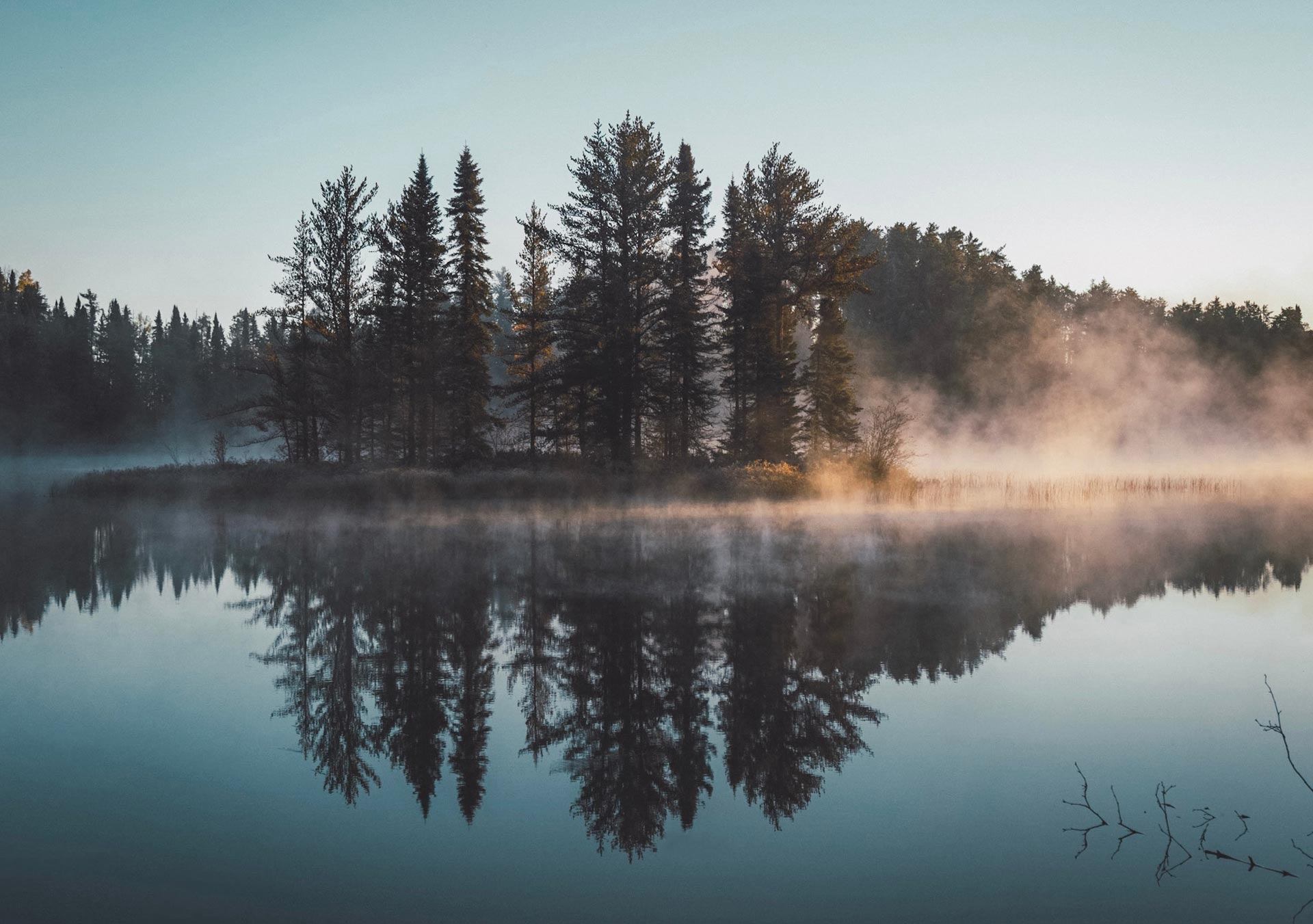 lake with trees reflected in the water and smoke covering the land on the other side