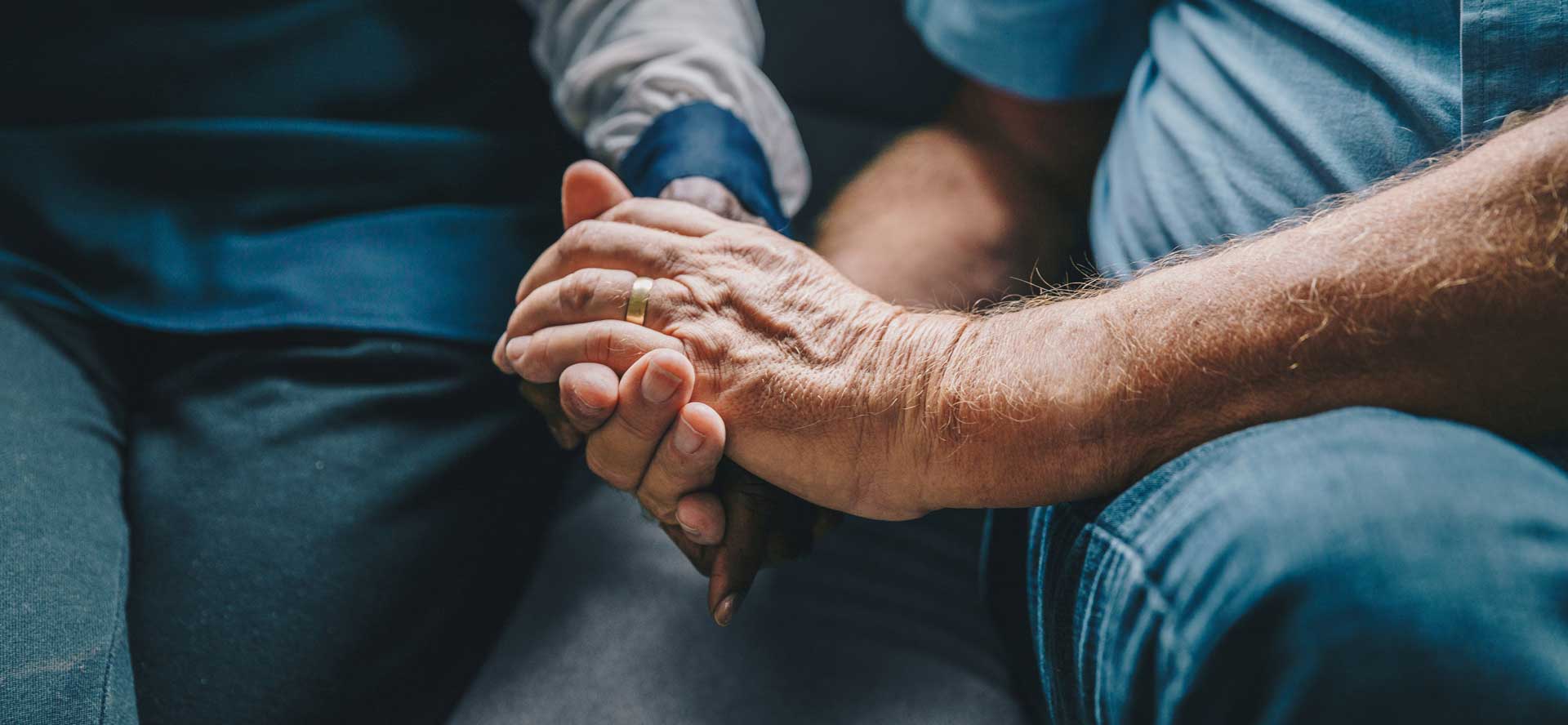 older man's hand holding woman's hand on couch