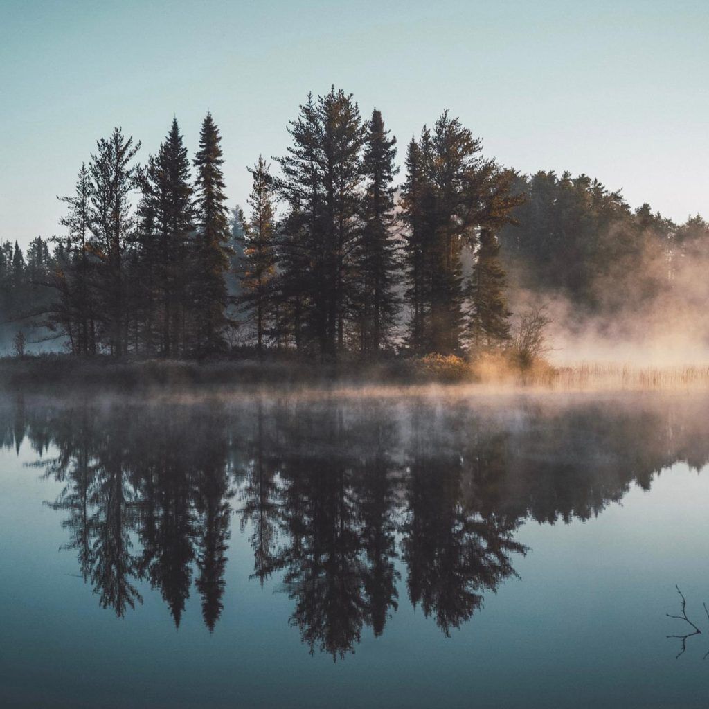 lake with trees reflected in the water and smoke covering the land on the other side